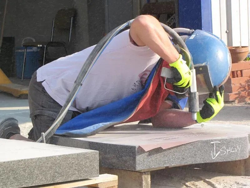 Artisans marbriers réalisant une gravure au sablage sur une plaque en granit