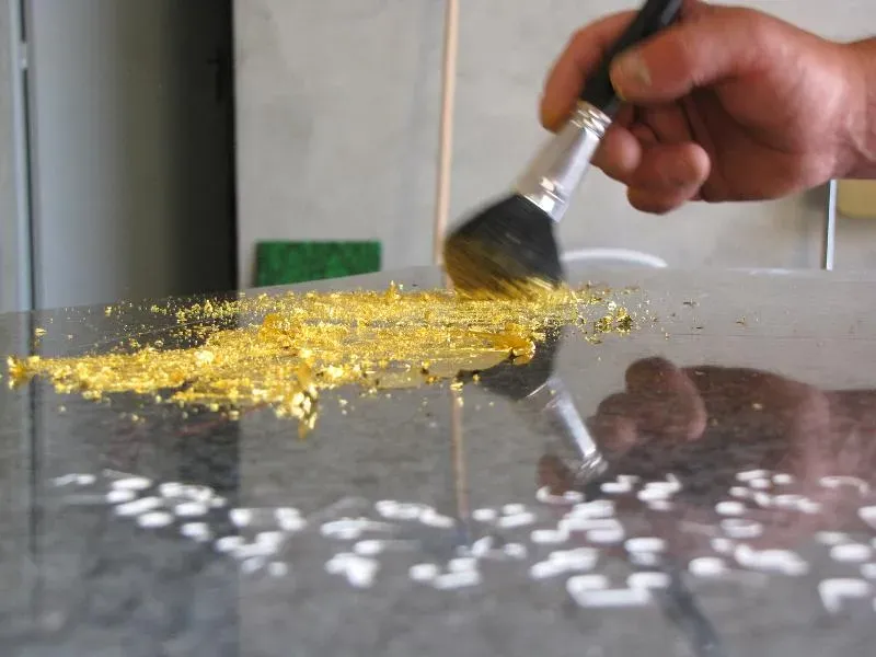 Application de feuilles d'or au pinceau sur une gravure funéraire