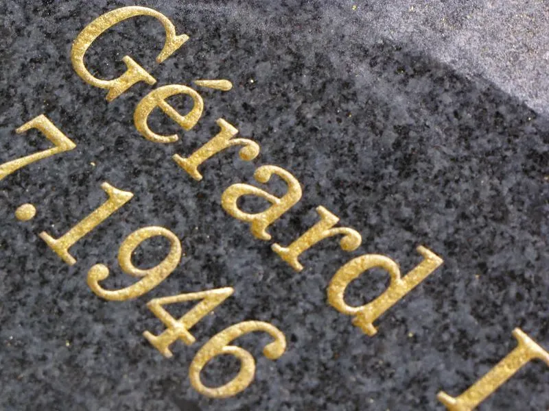 Gros plan sur des lettres et dates dorées à la feuille sur granit sombre